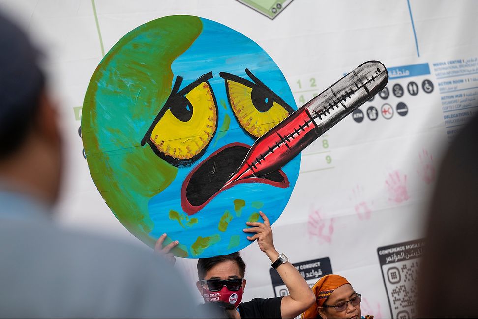 Protester holds up cartoon of an earth suffering from high temperature, as if it had a fever.