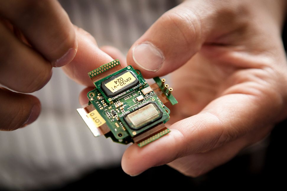 One hand holds a brain implant (a type of circuit board). Quadriplegics can use this to control a robotic arm.