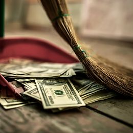 US dollar bills on the floor are swept up with a broom and dustpan.