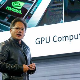 A man speaks on a stage in front of a large screen displaying Nvidia and GPU computing.