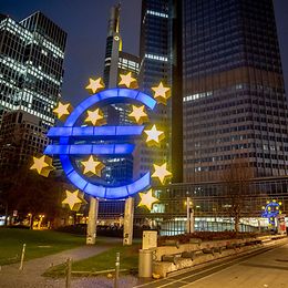 The ECB building in Frankfurt with an illuminated euro sculpture in the foreground.