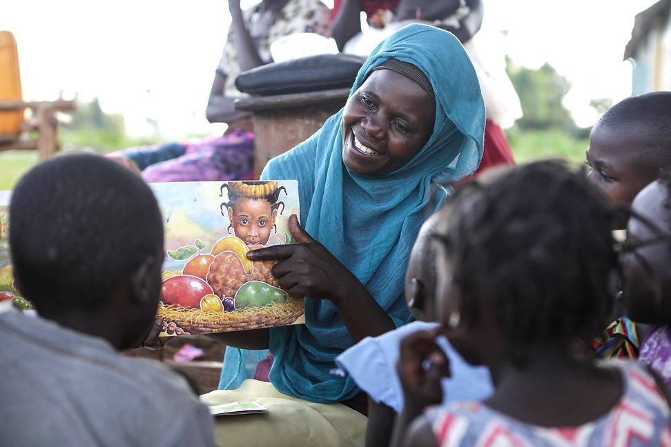 A volunteer showing a picture with fruits to the children