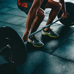 Ein Sportler hebt in einem Fitnessstudio eine Hantel mit Gewichten vom Boden ab