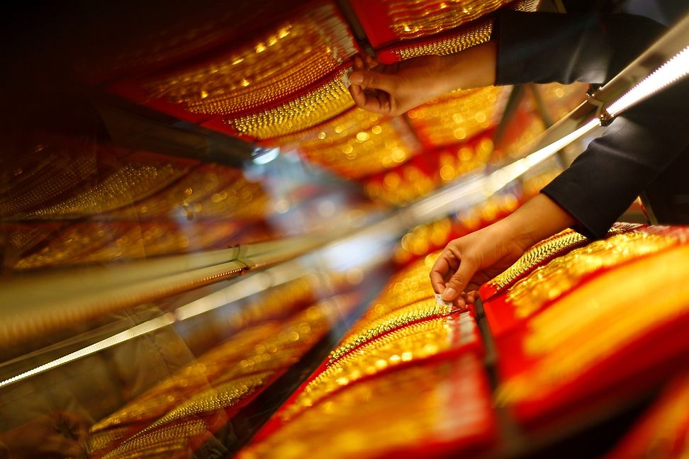 Eine Mitarbeiterin arrangiert goldene Schmuckstücke in einem Schaufenster in China
