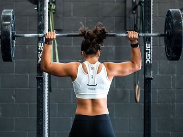 A person in sportswear in a gym lifting a barbell with heavy weights over their shoulders