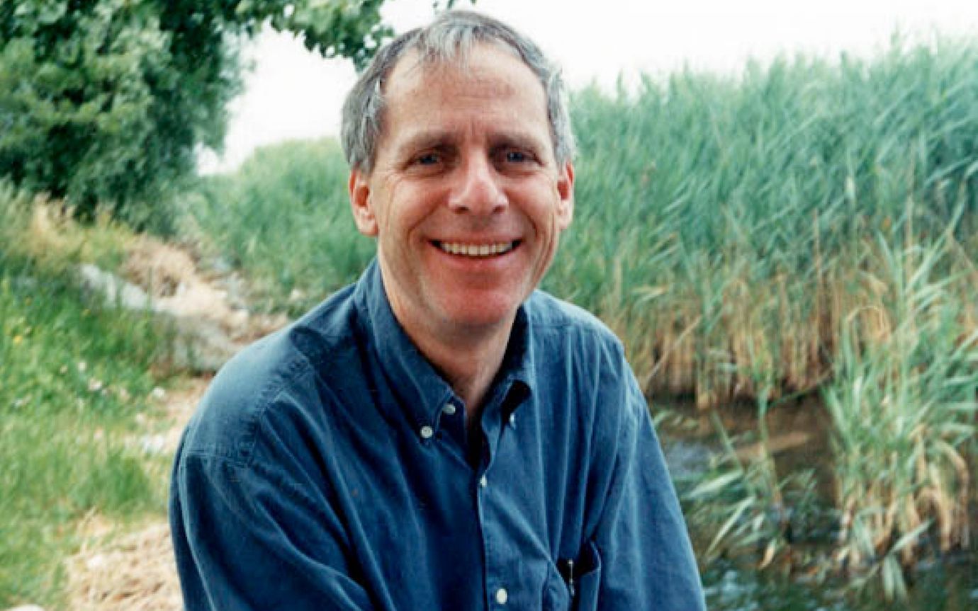 A man in a button-down shirt in the outdoors smiles into the camera. The image quality indicates that the image is not digital.
