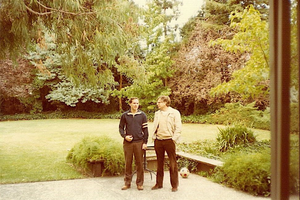 Two men are standing in a yard talking. The quality of the image shows that it is not digital.