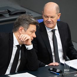 Zwei Männer mit Krawatte bei einer Konferenz in einem Auditorium auf ihren Plätzen.