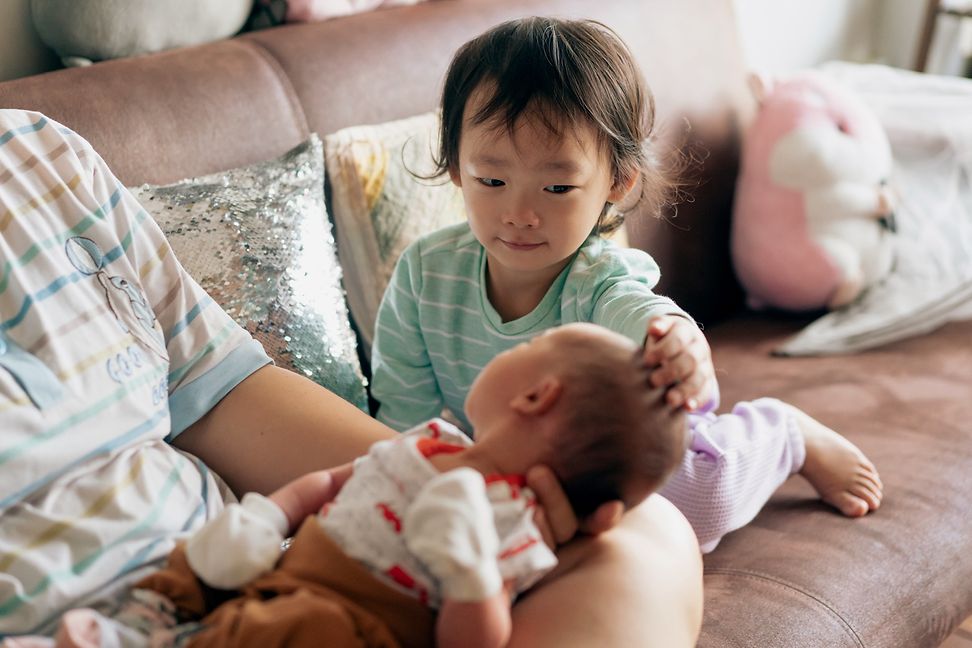 Ein Kleinkind begrüsst sein neues Geschwisterchen, ein neugeborenes Baby