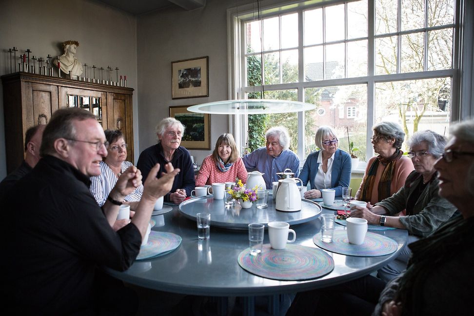 People in a domestic setting sitting around a table chatting over coffee and tea