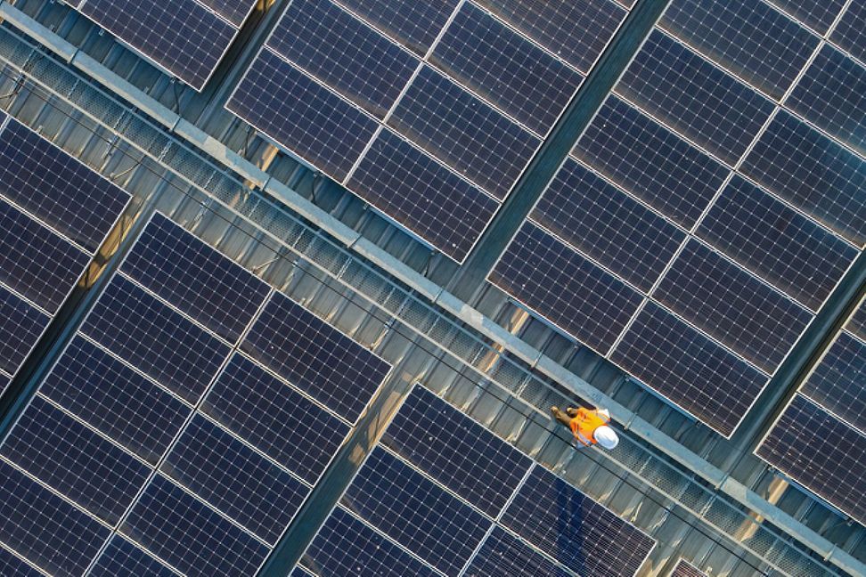 Arbeiter mit Helm von oben auf einem Dach voller Solarenergiezellen 