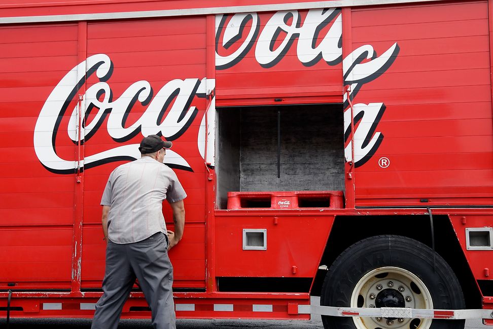 A man lifts something out of a van with a Coca-Cola logo