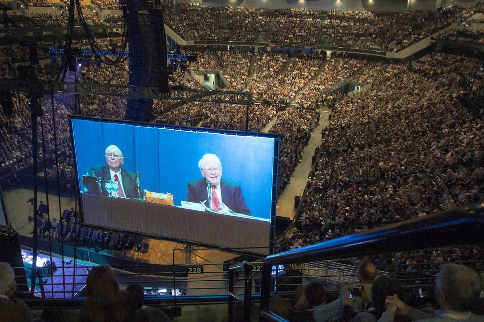 A big event with two elderly gentlemen on a podium, projected on a big screen into the hall