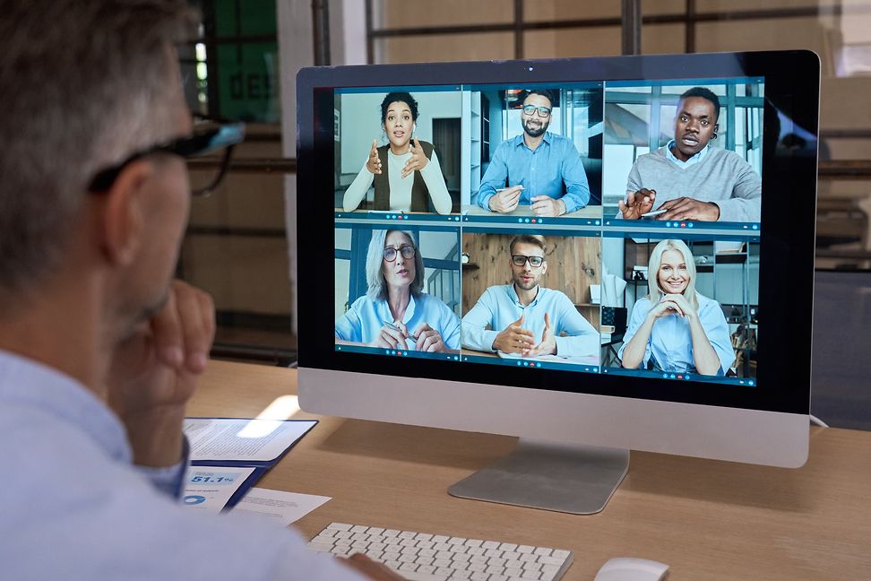 During a video meeting, a male employee looks at a screen showing the participants of the meeting.