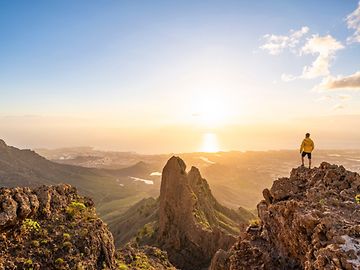 Eine Person steht auf einem Berg und blickt bei Sonnenuntergang in die Ferne.