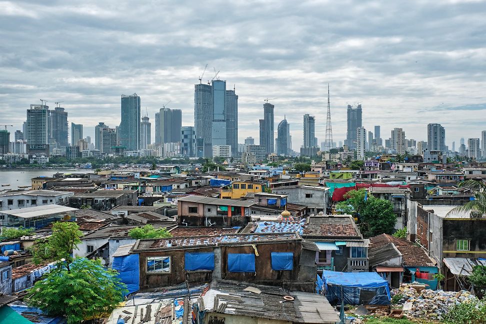 The skyline of a large city in the distance and simple huts and dwellings in the foreground