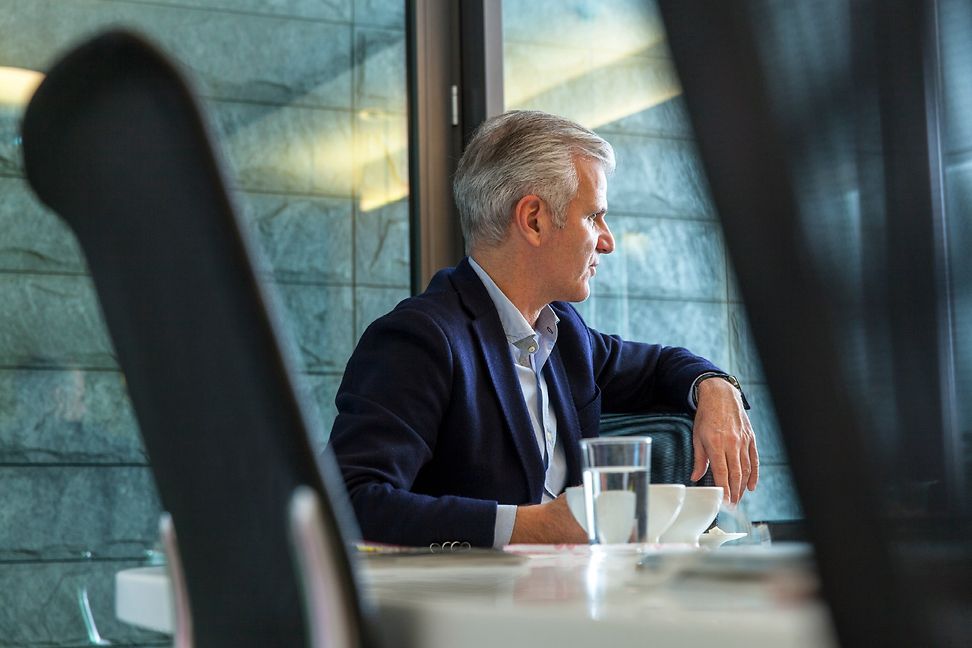 A grey-haired businessman looks out of the window of a modern office building.