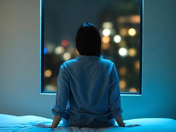 Frau sitzt nachts auf Bett und schaut aus Fenster