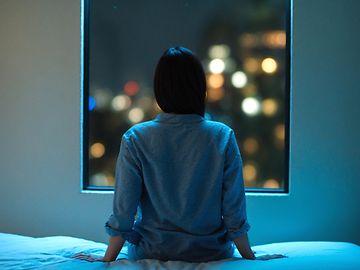 Woman sits on bed at night and looks out of the window