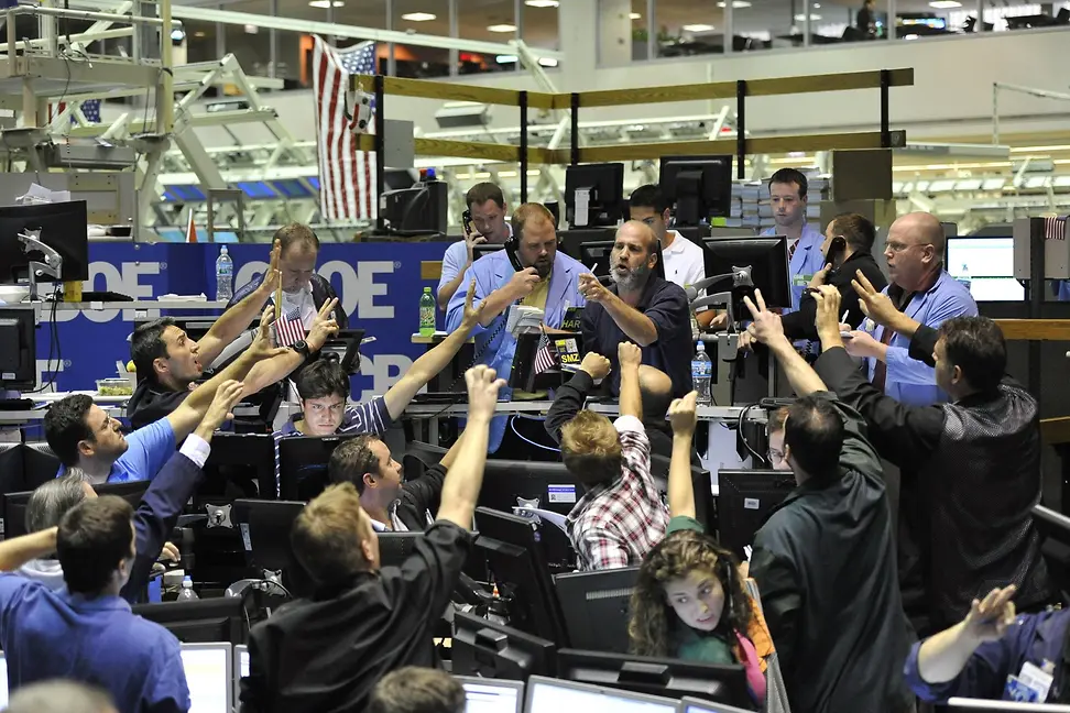 People, some in blue coats, look at computer screens or talk animatedly on the phone while raising their hands to a man.