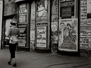 Schwarzweiss-Foto einer Frau vor einer Wand voller Posters in den 1950ern 